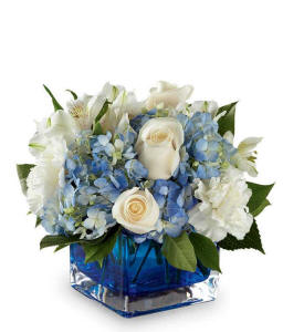 White carnations, white roses, white alstroemeria and blue hydrangea in a blue cube vase