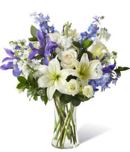 White lilies with blue accents arranged in a tall clear vase