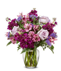 Lavender roses and purple blooms with greenery in a clear glass vase