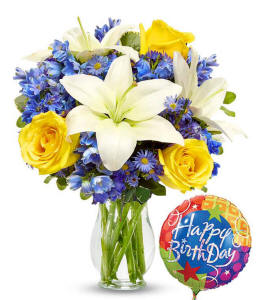 Yellow roses with blue delphinium and white lilies with a birthday balloon