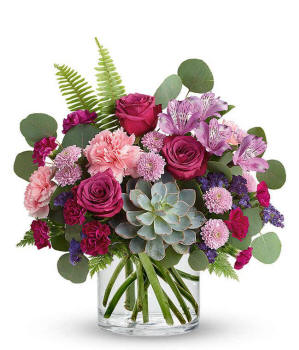Floral arrangement featuring a succulent plant, pink carnations, purple mini carnations, dark pink roses (in deluxe and premium versions), purple statice, purple alstroemeria, lavender button mums, seasonal greenery in a glass vase