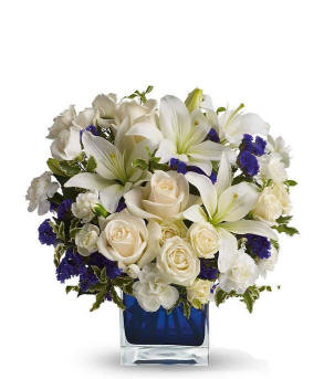 Creme roses, creme spray roses, white Asiatic lilies, white miniature carnations, and purple statice in a blue cube vase