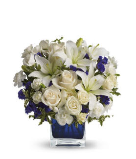 Clear Blue Skies Bouquet with creme roses, creme spray roses, white Asiatic lilies, white miniature carnations, purple statice, and a blue cube vase