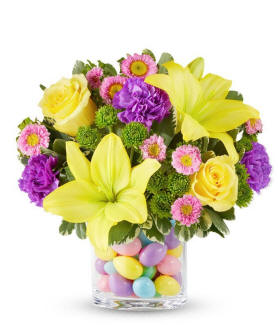 A clear vase with plastic Easter eggs and colorful Easter flowers