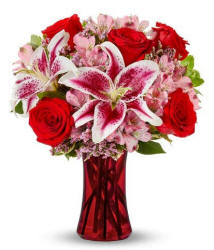A red vase filled with lilies and red roses