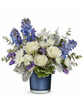 Fall for Me arrangement with creme roses, blue delphinium, white carnations, white cushion spray chrysanthemums, greenery, and a sapphire blue cylinder container