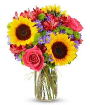 Bright yellow sunflowers with pink roses and greenery in a clear glass vase