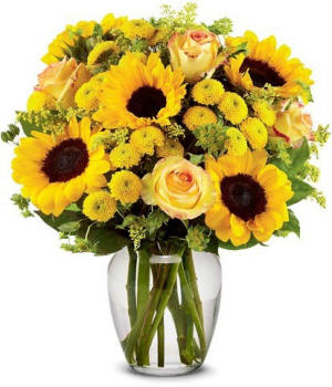 A clear glass vase filled with yellow sunflowers and roses